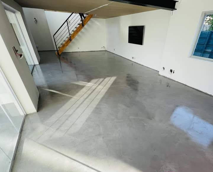 Grey concrete overlay floor in a bright double-volume room with a timber staircase