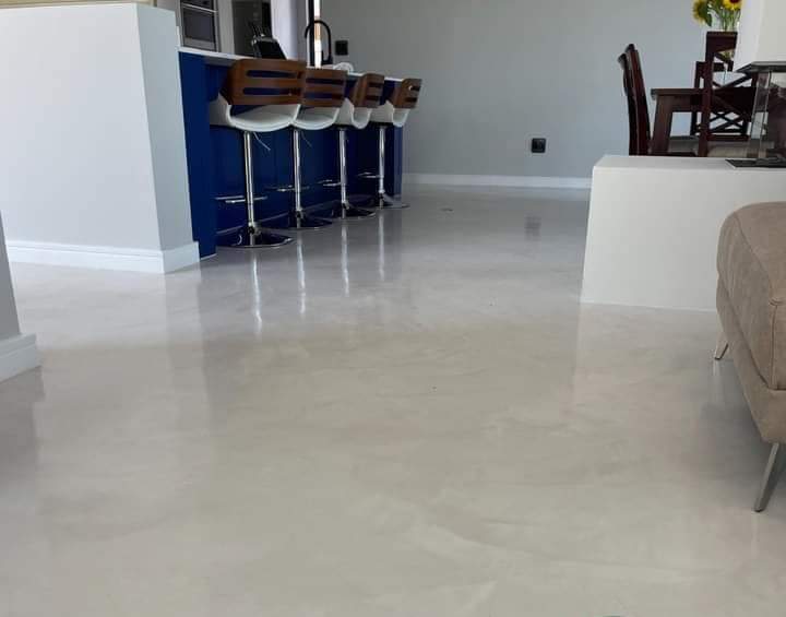 Pale, softly clouded screed floor in an open-plan kitchen with a navy island